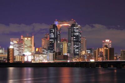 Illuminated umeda sky building in front of river against sky at dusk in city