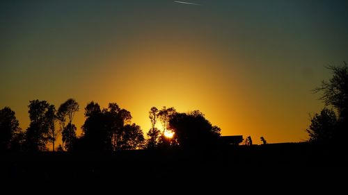 Silhouette trees on landscape against sky at sunset