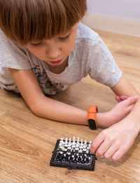 Cute boy playing chess on floor at home