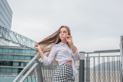 Young woman licking lollipop in city against sky