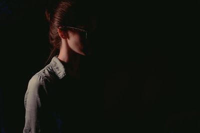 Close-up of young woman standing against black background