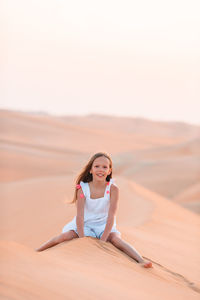 Portrait of woman sitting on sand in desert against sky