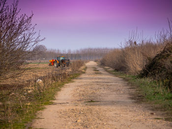 Dirt road amidst field against sky