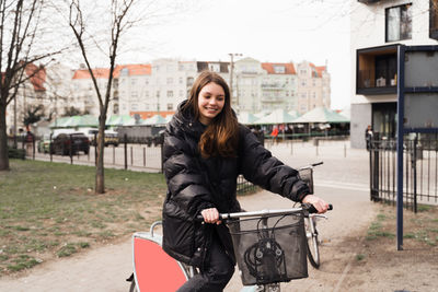 Happy young woman with bicycle standing on footpath