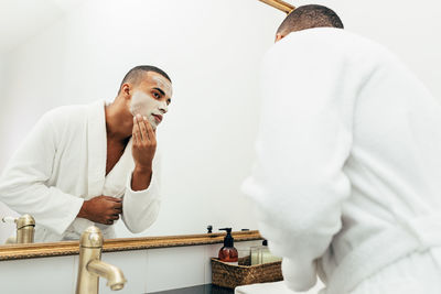 Man applying moisturizer on face while standing at bathroom