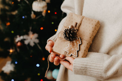 Girl hands holding small gift in her hands. close up. decorated christmas tree on background. 