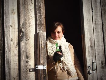 Woman holding bottle of drink amidst wooden doors