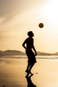 Full length of silhouette man playing ball on beach against sky during sunset