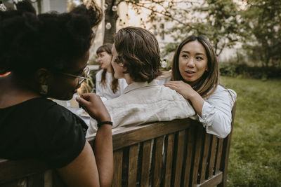 Smiling female talking to friend behind partner during social gathering