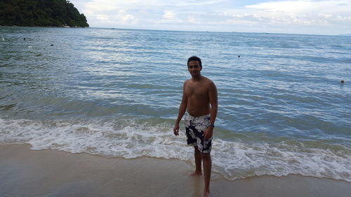 Full length of shirtless man standing at beach against sky