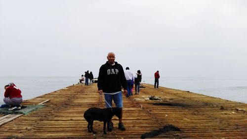 Man standing with dog on pier against clear sky