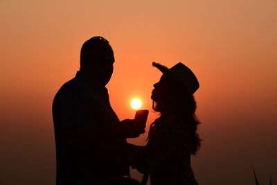 Silhouette man and woman standing against orange sky during sunset