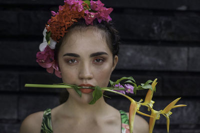 Portrait of young woman with flower in mouth standing against wall