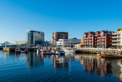 Boats in river by buildings in city against clear blue sky