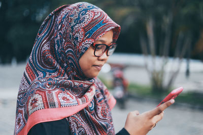 Side view of smiling young woman using phone on footpath