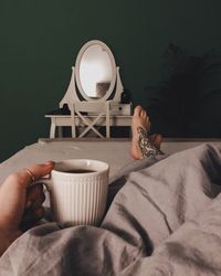 Low section of woman holding coffee cup while lying on bed at home