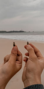 Close-up of hands on sea shore against sky