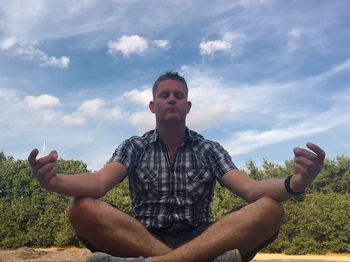 Low angle view of man meditating at beach against sky