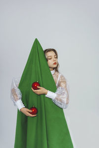 Teenage girl standing with artificial christmas tree and decoration against white background