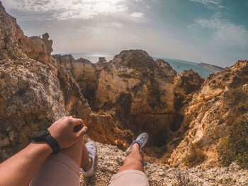 Low section of person on rock in mountains against sky