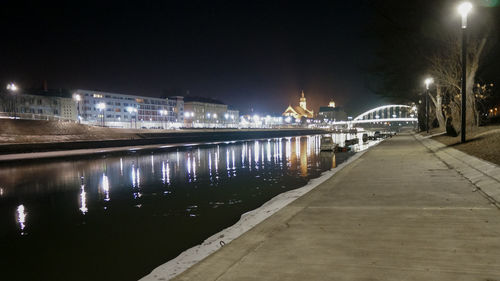 Illuminated city by river against sky at night