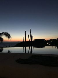 Silhouette wooden posts on beach against clear sky at sunset