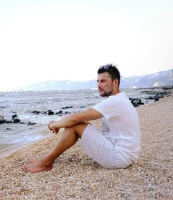 Side view of young man sitting on beach