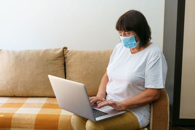 Serious woman in protective mask uses laptop, checks email on internet while