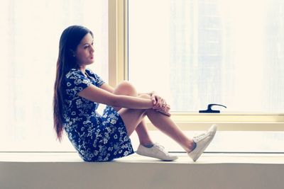 Side view of young woman sitting on window