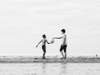 Full length of friends standing on beach against sky