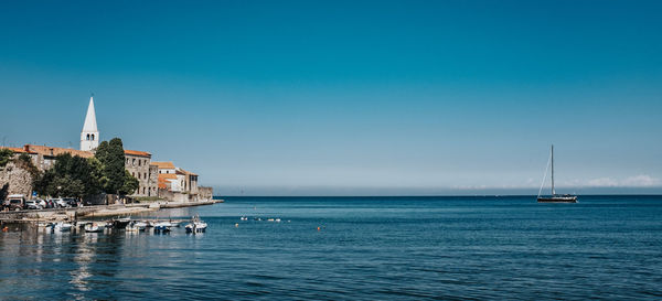 Sailboats in sea by buildings against clear blue sky