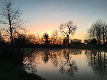 Silhouette trees by lake against sky during sunset