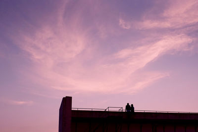 Low angle view of silhouette man standing on railing against sky