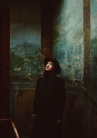 Woman looking up while standing against old wall