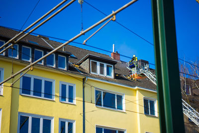 Low angle view of firefighter on cherry picker near building against clear blue sky