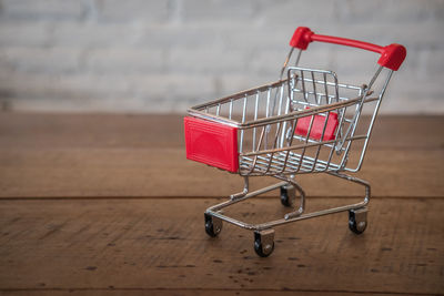 Close-up of small shopping cart on wooden table against wall