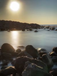 Rocks at sea shore against sky during sunset
