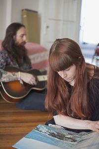 Young woman looking at a record album while her boyfriend plays guitar