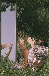 Rear view of woman praying in front of mirror while sitting on field