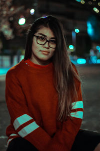 Portrait of young woman standing against illuminated wall