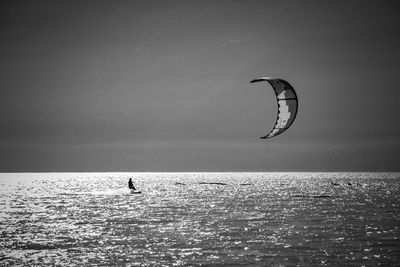 Person paragliding in sea against sky