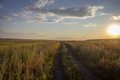 Road amidst field against sky during sunset