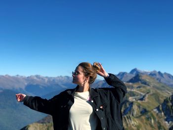 Woman with arms raised standing against mountain and clear blue sky