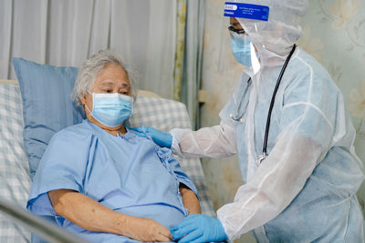 Doctor wearing protective suit consoling patient at hospital