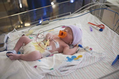 High angle view of newborn baby boy with medical equipment sleeping in crib at hospital