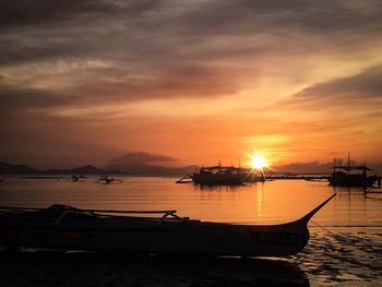 Silhouette boats moored on sea against orange sky