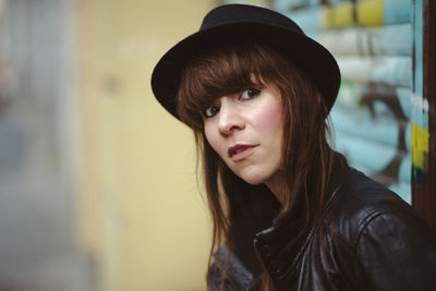 Portrait of woman wearing hat against graffiti shutter in city