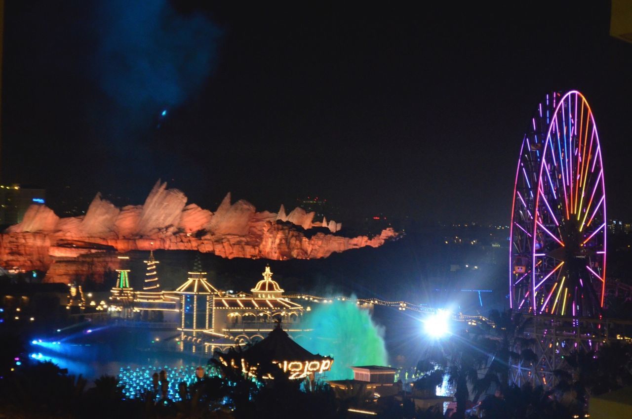 illuminated, night, arts culture and entertainment, built structure, building exterior, architecture, clear sky, city, ferris wheel, sky, amusement park, firework display, long exposure, glowing, celebration, amusement park ride, copy space, blue, travel destinations, outdoors