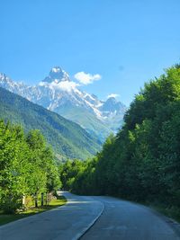 Road amidst snowcapped mountains against clear blue sky