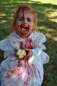 Portrait of girl in halloween costume eating apple while standing on field